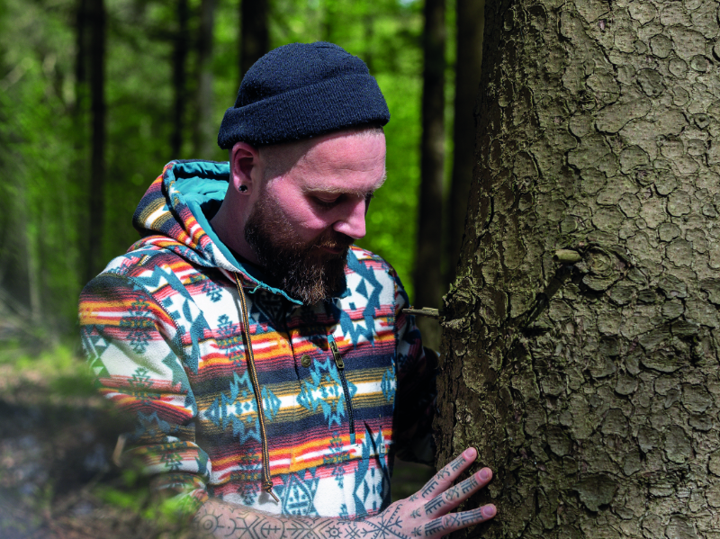 Mann mit Mütze und Kapuzenpullover umarmt Baum im Wald